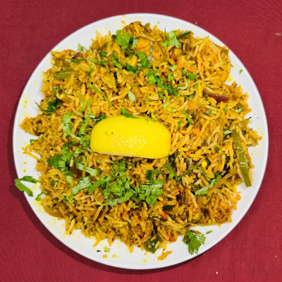 A white plate of chicken biryani, garnished with fresh cilantro and a lemon wedge, on a red tablecloth.