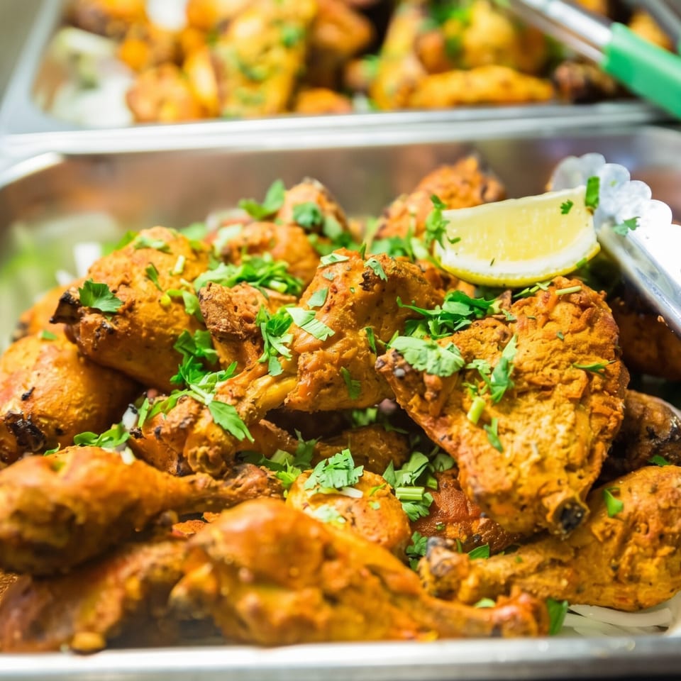 Close-up of golden-brown chicken drumsticks garnished with fresh cilantro and a lemon wedge.